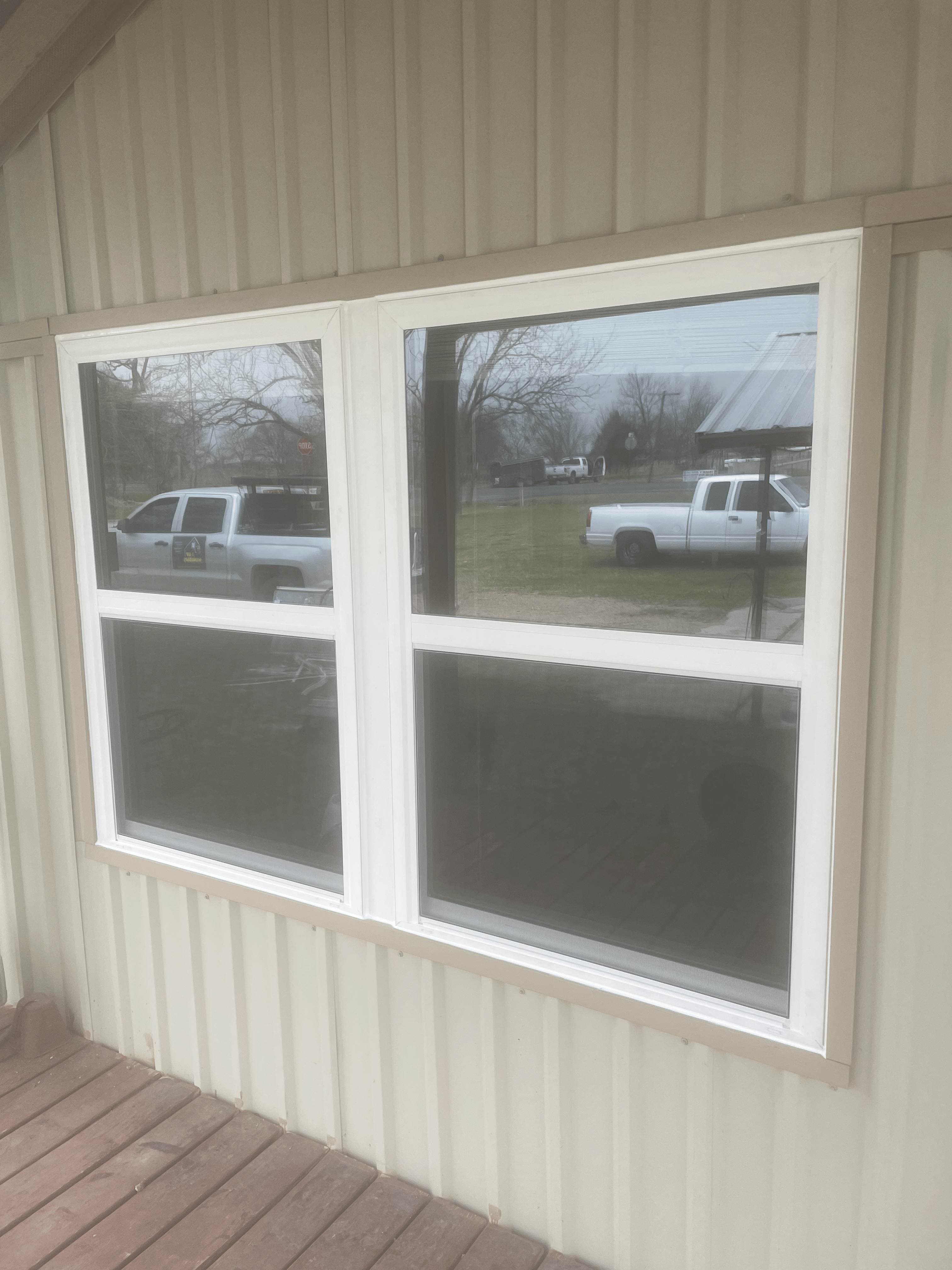 Double white frame single-hung windows on tan corrugated metal siding with porch view