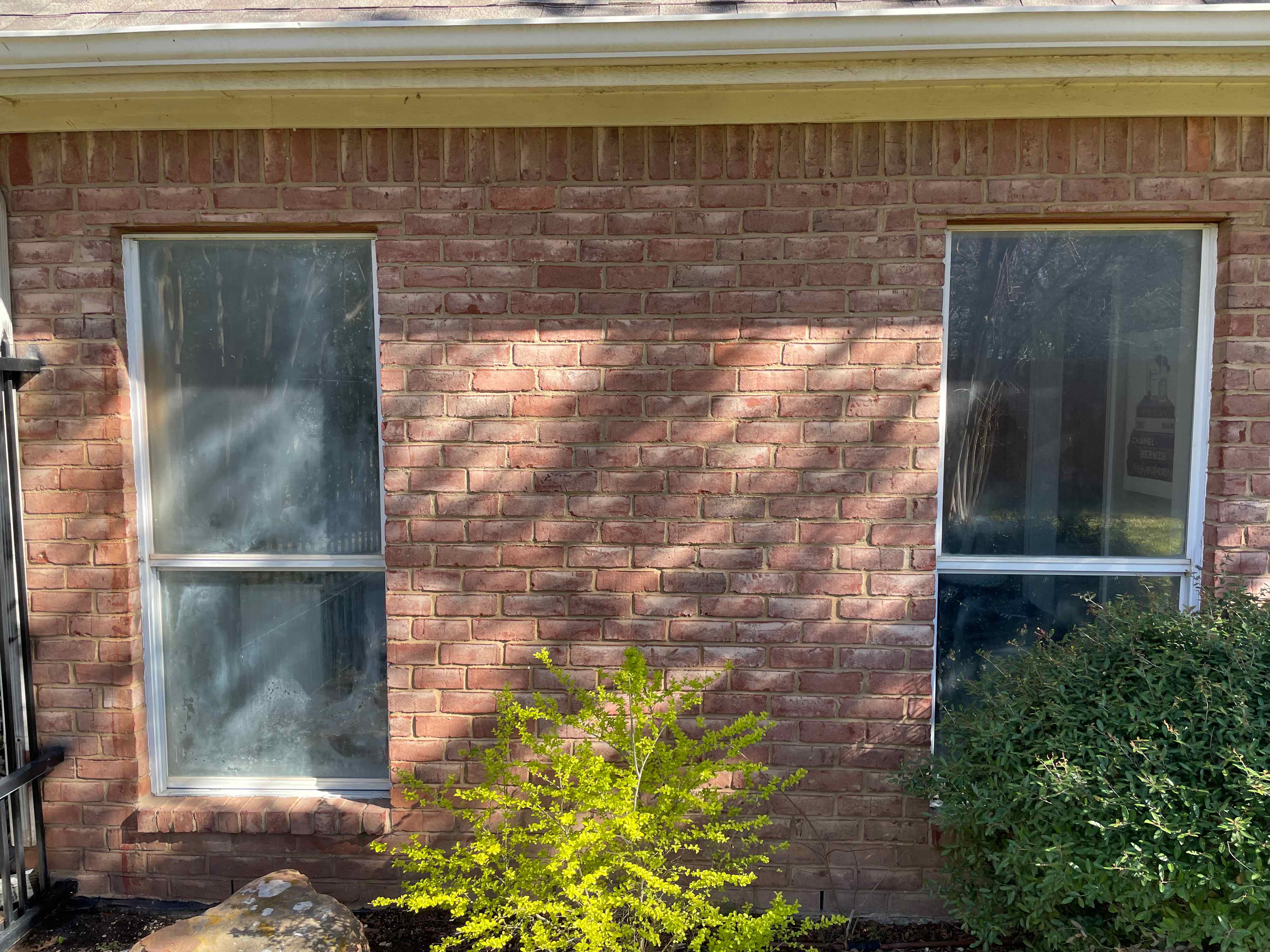 Bronze-framed replacement window on red brick exterior with landscaping
