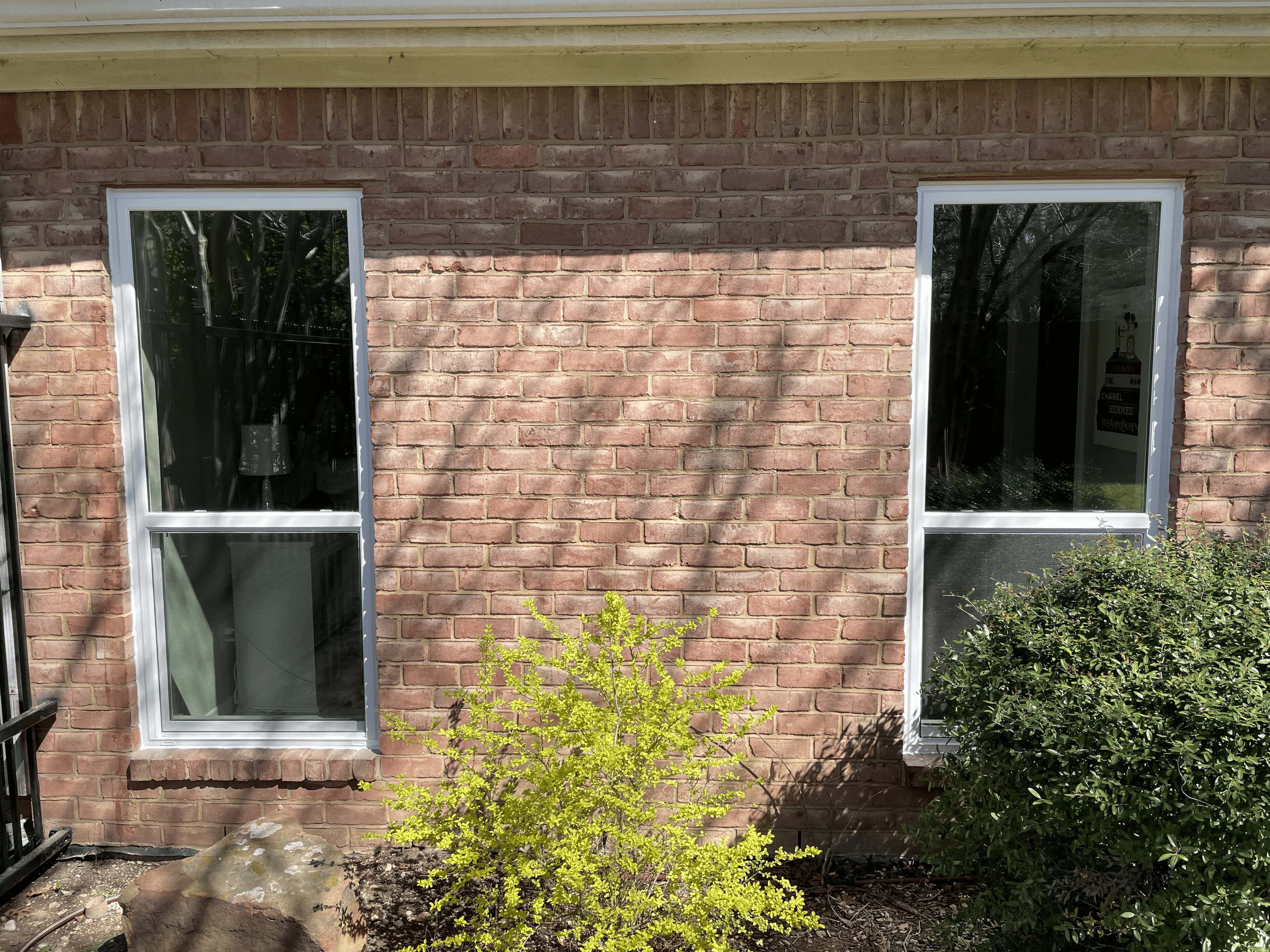 White frame single-hung windows installed on salmon pink brick home with landscaping
