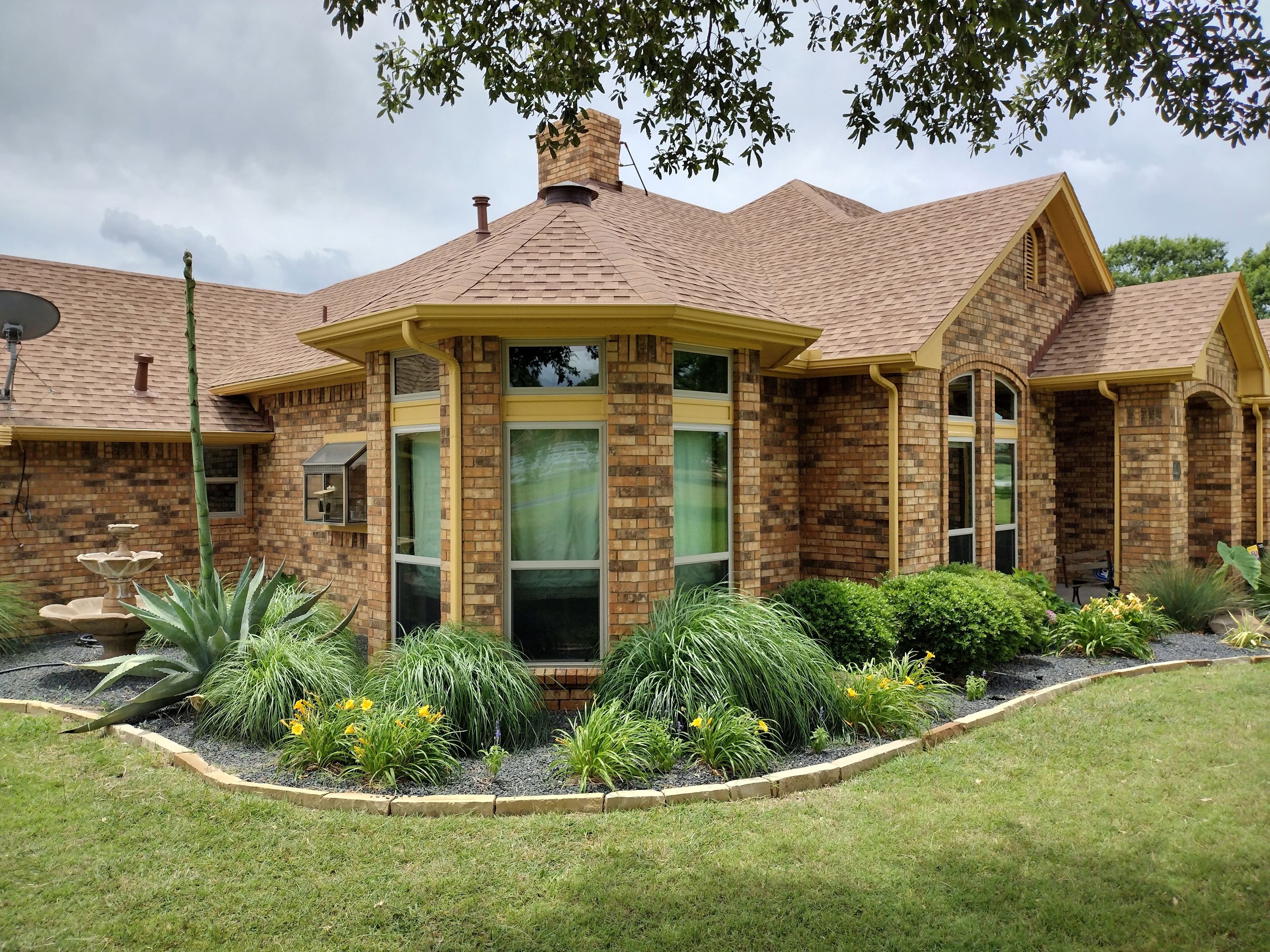 Beautiful ranch home with bay windows and yellow trim surrounded by professional landscaping